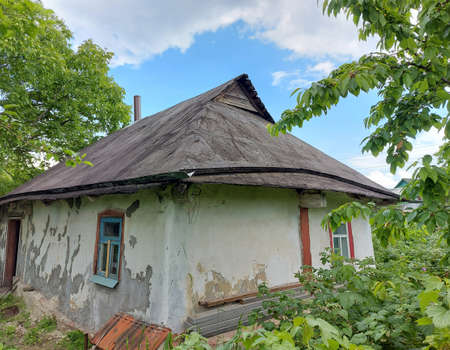 A white hut with a black roof among green trees under a blue sky with white cloudsの写真素材