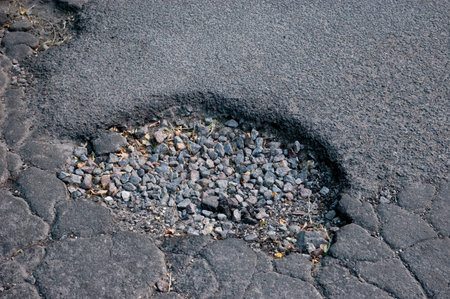 Pothole in asphalt filled with gravel, symbol of neglect and urban decay. Rough road surface with broken pavement and temporary repair in city environment.の写真素材
