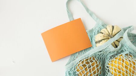 Autumn flat lay composition with orange pumpkins in mesh shopping bag on white background. Creative autumn, thanksgiving, fall, halloween concept in zero waste style. Top view, copy spaceの写真素材