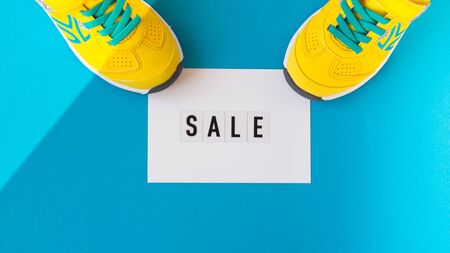 Pair of yellow shoes on blue background hold a white card text sale.Top view,flay lay,sale concept,...