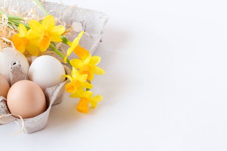 white eggs on a white background. brown and white eggs in a package with yellow spring flowers daffodils. Easter background, place for an inscriptionの写真素材