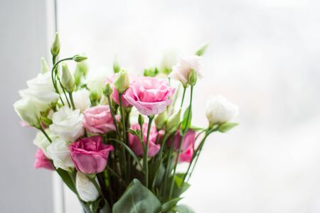 Defocused view. Bouquet of pink and white eustoma in a glass vase on the windowsill of the loggia. Flowers in a vase on the windowsill of the balcony.の写真素材