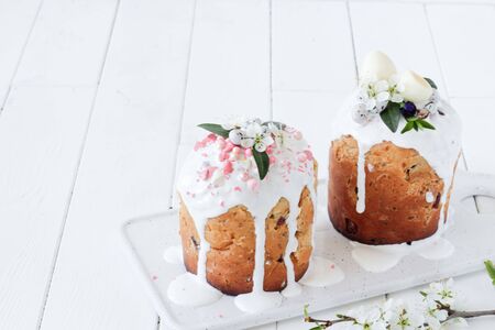 Easter Orthodox sweet bread, two Easter cakes decorated with flowers and sweets on a white marble...