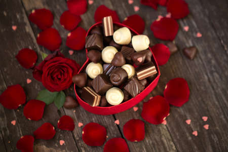 Red roses and chocolate pralines in heart shaped gift box backgroundの写真素材