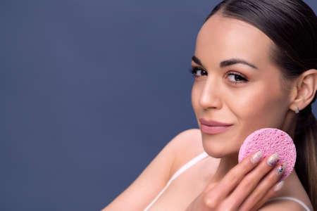 Beautiful young woman with clean fresh skin touch own face. Facial treatment. Cosmetology, beauty and spa. Smiling young girl cleaning her face with cotton discの写真素材