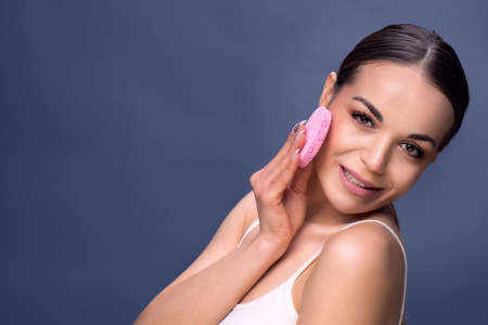 Young woman using a cotton pad to remove her make-up .Smiling young girl cleaning her face with cotton discの写真素材