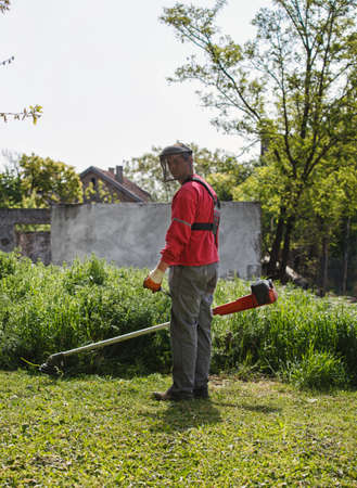 man cutting grass with hand trimmer in yard