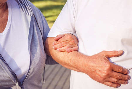 Close up of hands of romantic senior couple during walk in park on sunny dayの写真素材