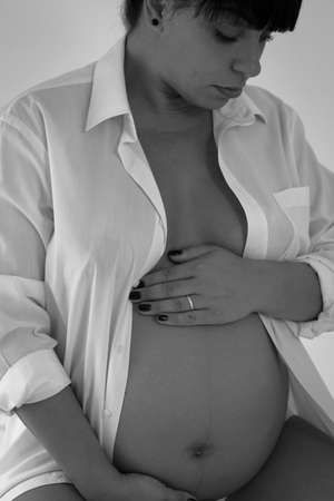 Beautiful pregnant female cuddling belly in bedroom at home black and white