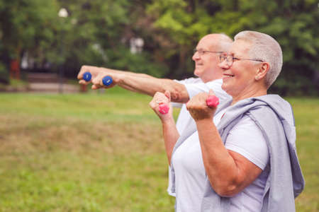 Together we workout better - Smiling senior man and woman practice with dumbbells in a parkの写真素材