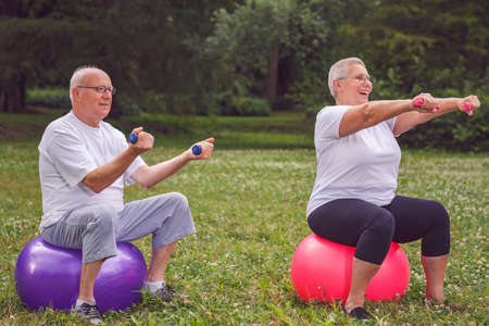 Smiling senior sports woman and man sitting on fitness ball with dumbbellsの写真素材