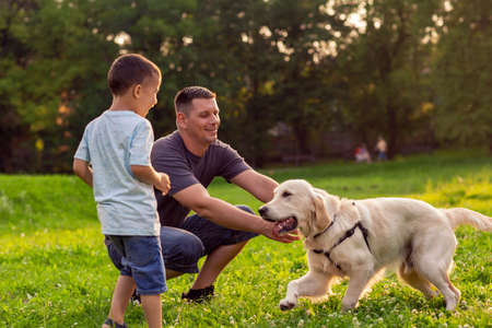 Beautiful happy family is having fun with golden retriever - Happy father and his son playing with dog in parkの写真素材