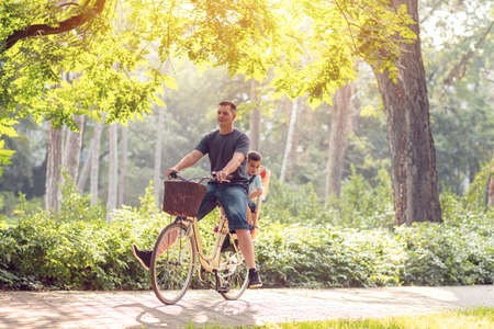 Smiling active father with kid on bicycles having fun in park. Family sport and healthy lifestyleの写真素材