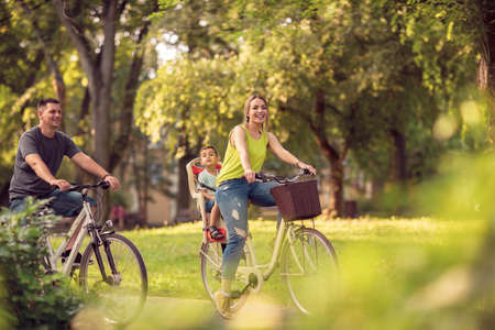 Smiling active father and mother with kid on bicycles having fun in park.の写真素材