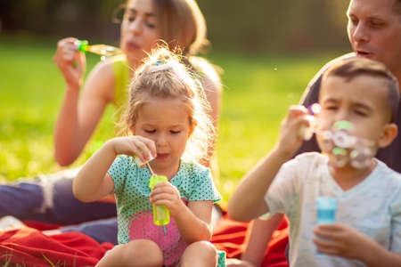 cute little girl blows soap bubbles with her family in the parkの写真素材