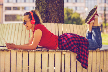 Young woman listening to the music from a smartphone lying in a bench of a parkの写真素材