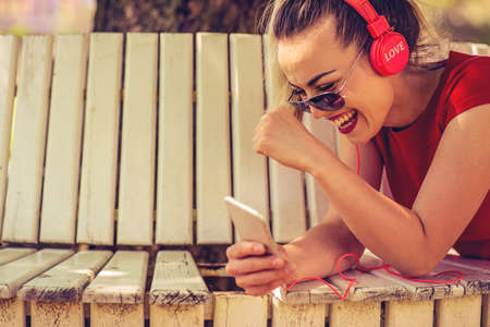 Happy young girl listening to the music from a smartphone lying in a bench of a park close upの写真素材