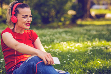 beautiful happy woman with earphones and smartphone listening to music on grass in parkの写真素材