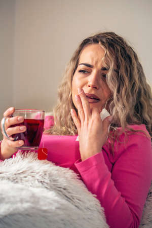 Sick woman in bed, calling in sick, day off from work. Drinking herbal tea. Vitamins and hot tea for flu. Woman Caught Cold. Virus.の写真素材