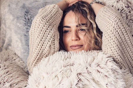 Cheerful young woman covering with a blanket in the bedの写真素材