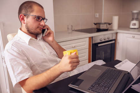 Young freelancer having break and talking on his phone at home