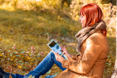 Young woman using tablet outdoor in autumn parkの写真素材