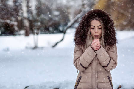 young woman in winter snow day blow on her cold handsの写真素材