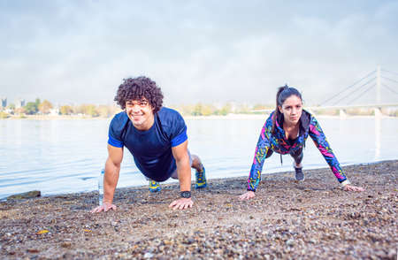 Happy Sportswoman and sportsman doing push-ups outdoors