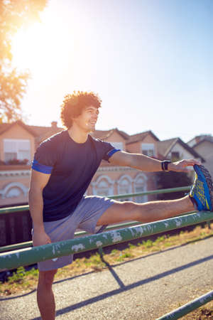 Smiling athletic runner doing stretching exercise, preparing for workout in the park