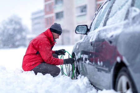 Young man installing snow chain on car