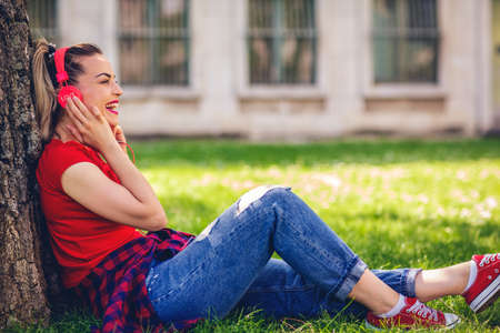 Young smiling girl listening to music in city parkの写真素材