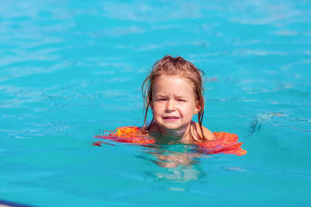 Cute happy child girl learning swimming with inflatable armbands