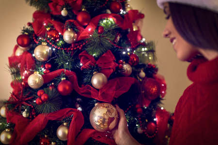 Happy woman in Santa hats placing a ornament on a Christmas tree. の写真素材