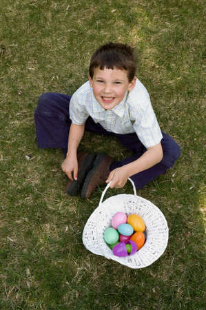 a boy sits on the lawn showing off his white easter basket full of colorful plastic eggs after an...