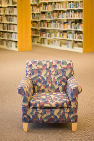 a reading chair in a library with book stacks in the backgroundの写真素材