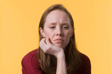 a sad depressed young woman with her hand on her chinの写真素材