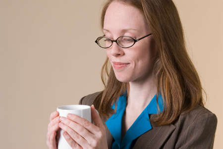 a young business woman looks down with pleasure at a mug of coffee she is holdingの写真素材