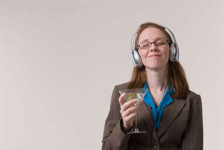 a young business woman relaxes with a martini and music after workの写真素材