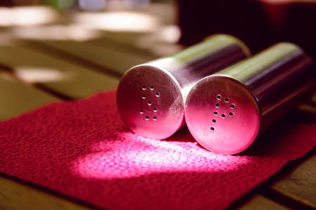Side view of salt and pepper metall bottles on red napkin on wooden tableの写真素材