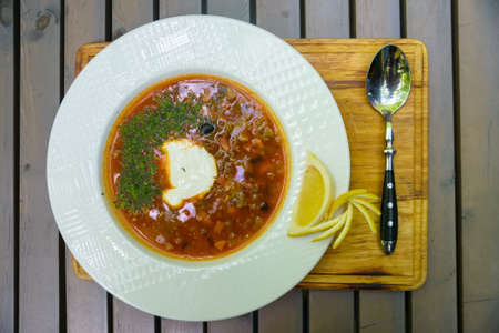 Russian traditional thick meat soup solyanka served on wooden table