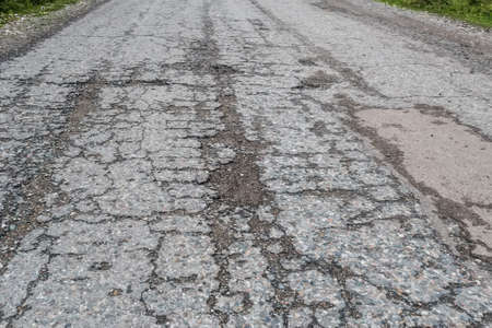 Damaged road with cracked asphalt blacktop with potholes and patchesの写真素材