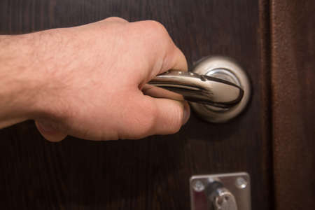 Closeup of hand holding metal silver doorknob on wooden door