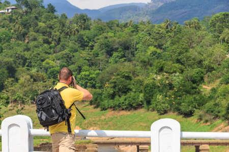 Male hiker with camera standing on edge of rockの写真素材