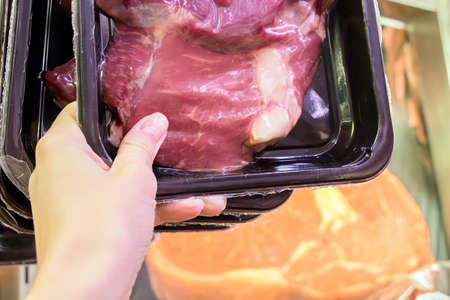 Woman holds raw meat in grocery storeの写真素材