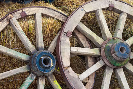 Two old wooden wagon wheels lean on hay stacks