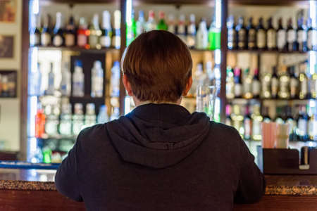 Back view young man sits at modern bar counterの写真素材