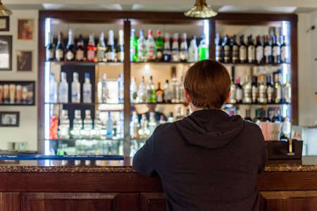 Back view young man sits at modern bar counterの写真素材