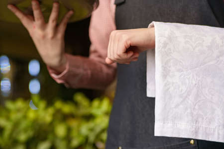 Yong waiter in tuxedo and gloves holding empty tray and napkin in restaurantの写真素材
