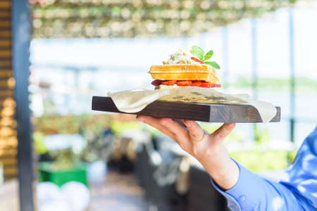 Close up hand holds Belgian waffles on trayの写真素材