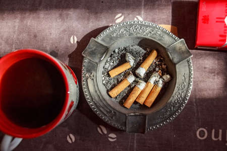 Cigarettes in black metal ash tray and tea mugの写真素材